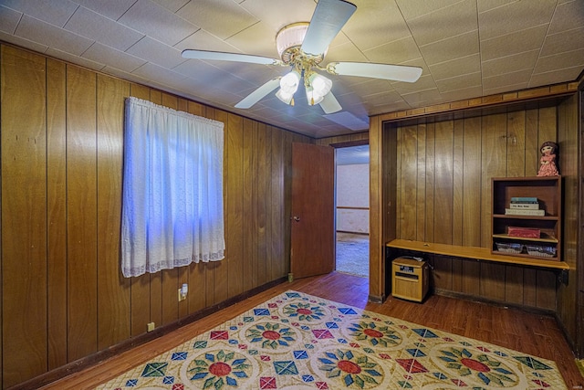 office area with wood walls, wood-type flooring, and ceiling fan