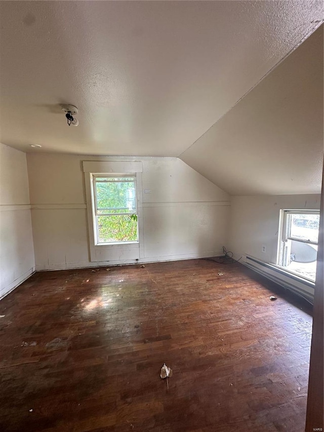 additional living space featuring baseboard heating, dark hardwood / wood-style floors, a textured ceiling, and vaulted ceiling