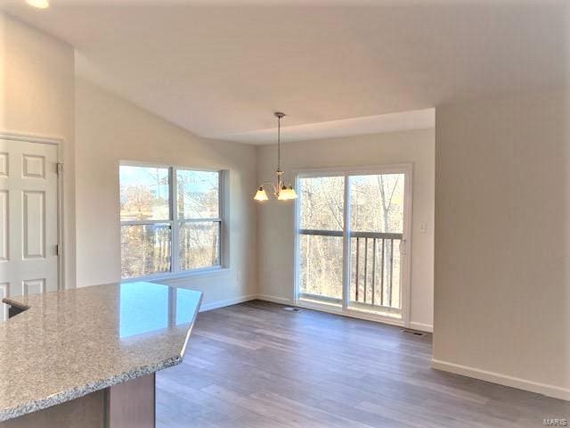 unfurnished dining area featuring a wealth of natural light, dark wood-type flooring, and an inviting chandelier