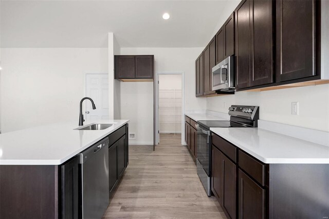 kitchen with light wood-type flooring, a kitchen island with sink, dark brown cabinets, sink, and appliances with stainless steel finishes