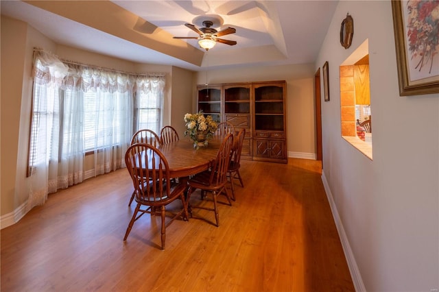 dining space featuring a raised ceiling, ceiling fan, and light hardwood / wood-style floors