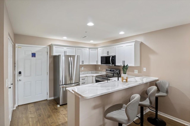 kitchen with light hardwood / wood-style flooring, a kitchen bar, stainless steel appliances, kitchen peninsula, and white cabinets