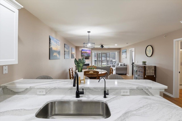 kitchen featuring hanging light fixtures, light stone counters, sink, wood-type flooring, and ceiling fan