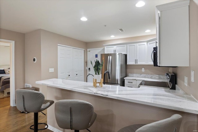 kitchen with a kitchen breakfast bar, wood-type flooring, appliances with stainless steel finishes, kitchen peninsula, and white cabinetry