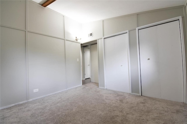 unfurnished bedroom featuring two closets, light carpet, and vaulted ceiling