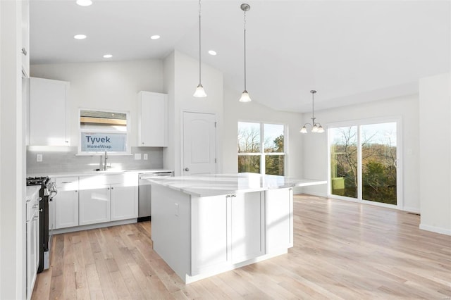 kitchen with light wood-type flooring, stainless steel appliances, decorative light fixtures, a kitchen island, and white cabinets