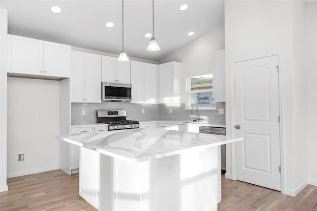 kitchen featuring a kitchen island, light stone counters, appliances with stainless steel finishes, lofted ceiling, and light hardwood / wood-style floors