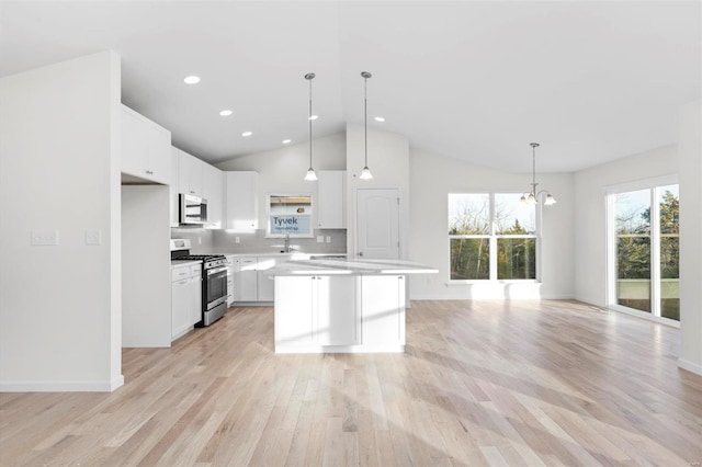 kitchen with white cabinets, hanging light fixtures, a center island, stainless steel appliances, and light hardwood / wood-style floors