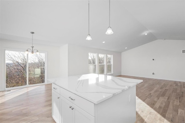 kitchen featuring white cabinetry, decorative light fixtures, a kitchen island, light stone countertops, and light hardwood / wood-style floors