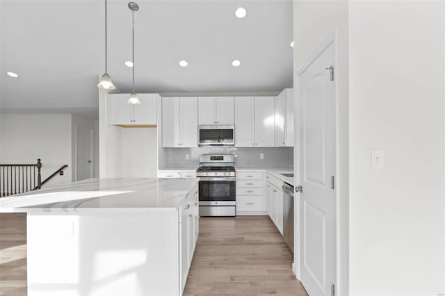 kitchen featuring pendant lighting, light hardwood / wood-style flooring, appliances with stainless steel finishes, a center island, and light stone counters