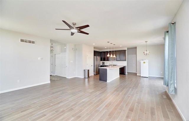 unfurnished living room featuring ceiling fan with notable chandelier and light hardwood / wood-style floors