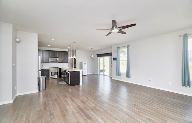 kitchen featuring a kitchen island with sink, ceiling fan, hanging light fixtures, appliances with stainless steel finishes, and light hardwood / wood-style floors