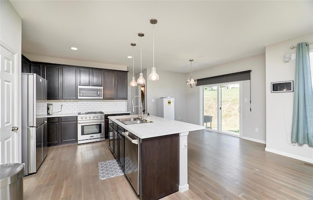 kitchen with light hardwood / wood-style flooring, decorative light fixtures, stainless steel appliances, sink, and an island with sink