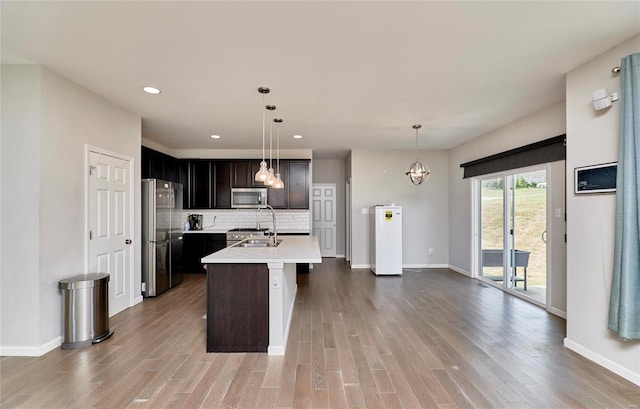 kitchen featuring backsplash, appliances with stainless steel finishes, sink, wood-type flooring, and an island with sink