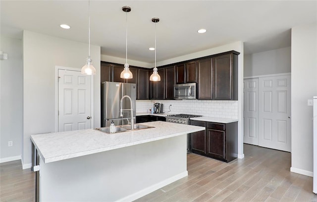 kitchen featuring dark brown cabinets, a center island with sink, pendant lighting, appliances with stainless steel finishes, and light wood-type flooring