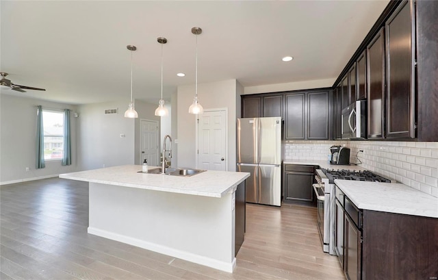 kitchen featuring light hardwood / wood-style flooring, appliances with stainless steel finishes, sink, ceiling fan, and a center island with sink