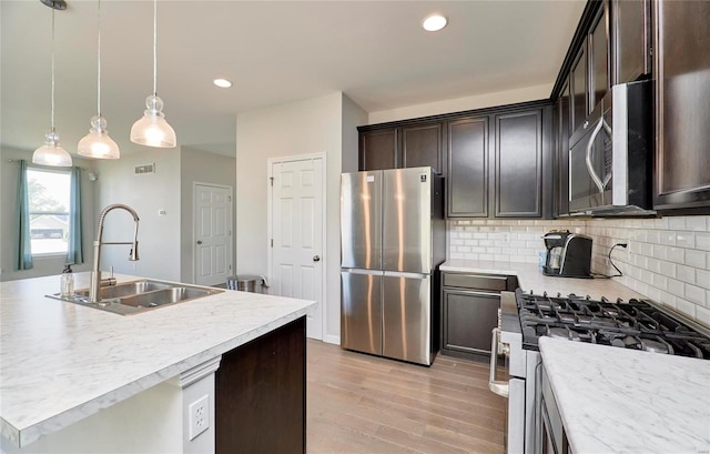 kitchen with tasteful backsplash, hanging light fixtures, stainless steel appliances, sink, and light wood-type flooring