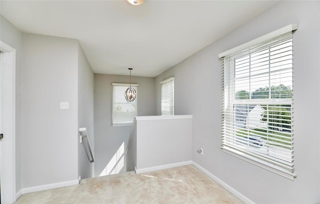 hall featuring plenty of natural light, a chandelier, and light colored carpet