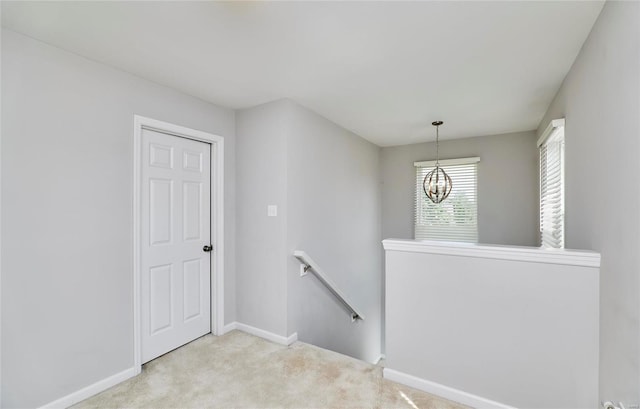 hallway with light carpet and a notable chandelier