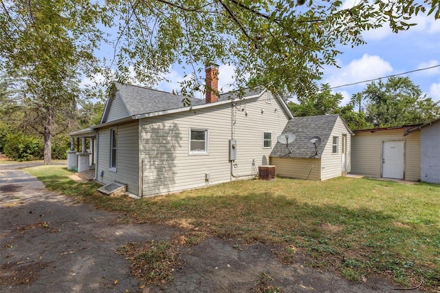 view of home's exterior featuring an outbuilding, a yard, a shingled roof, and a chimney