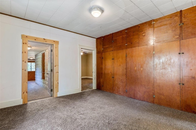 unfurnished bedroom featuring a closet, wooden walls, and carpet floors