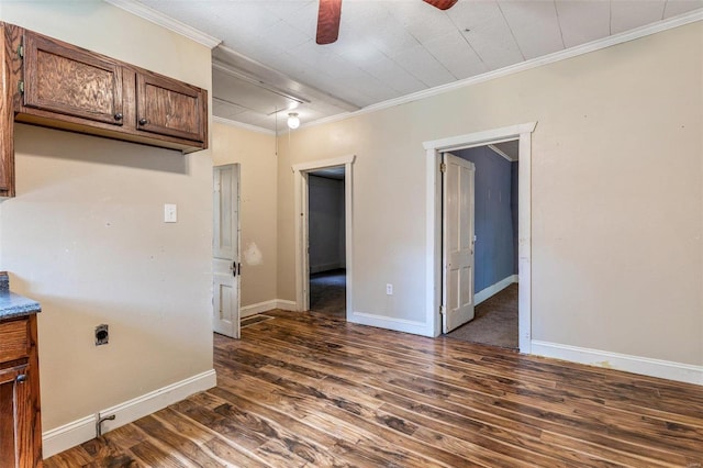 unfurnished room with attic access, dark wood-type flooring, crown molding, a ceiling fan, and baseboards