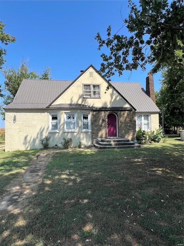 view of front facade with a front yard, a chimney, and metal roof