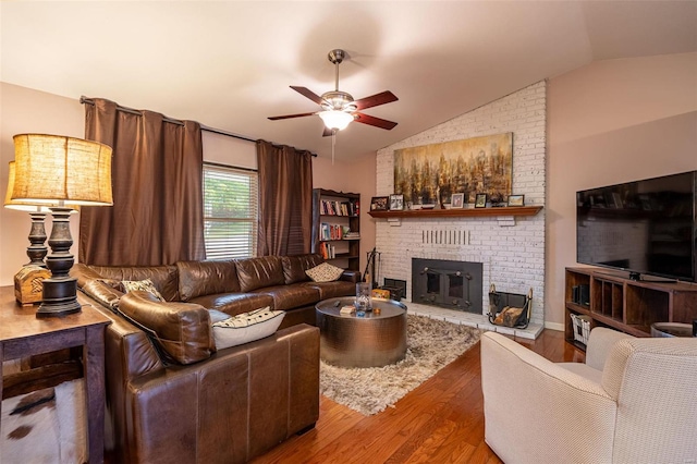 living room with vaulted ceiling, ceiling fan, wood-type flooring, and a brick fireplace