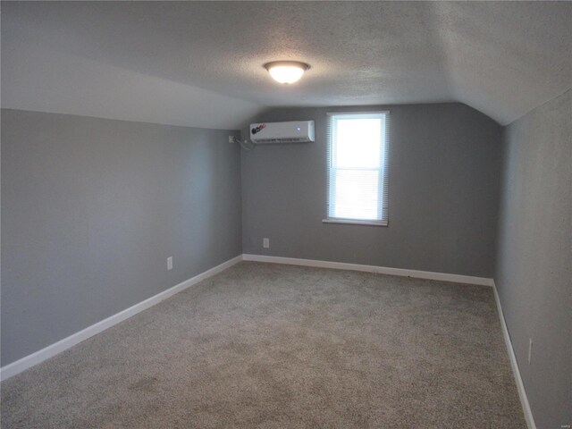 additional living space with a wall mounted air conditioner, a textured ceiling, lofted ceiling, and carpet flooring