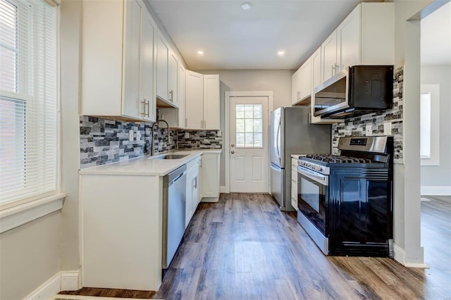 kitchen with hardwood / wood-style floors, backsplash, appliances with stainless steel finishes, sink, and white cabinets