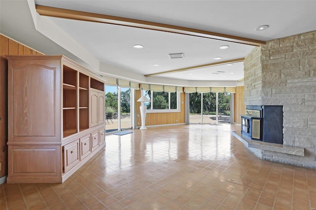 unfurnished living room with light tile patterned floors, beam ceiling, a fireplace, and wood walls