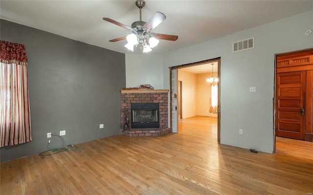 unfurnished living room featuring ceiling fan with notable chandelier, a fireplace, and light wood-type flooring