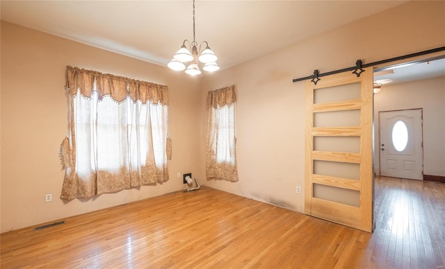 empty room with light hardwood / wood-style flooring, an inviting chandelier, and a barn door