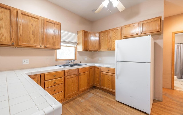 kitchen with light wood-type flooring, white refrigerator, sink, tile countertops, and ceiling fan