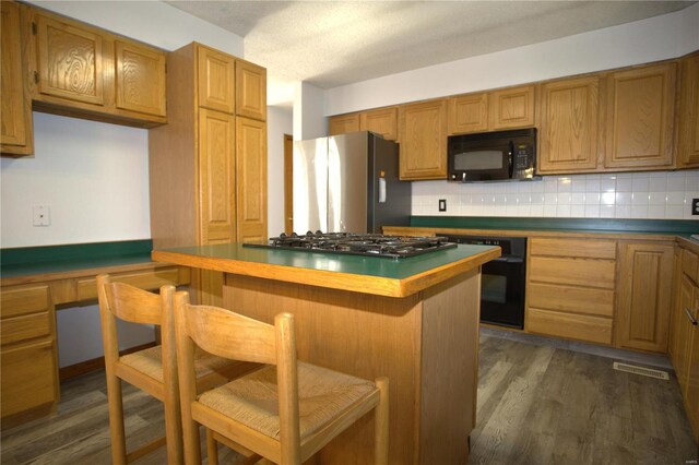 kitchen with backsplash, a breakfast bar area, dark hardwood / wood-style floors, and black appliances