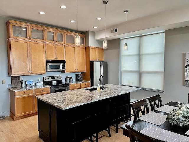 kitchen with light hardwood / wood-style flooring, stainless steel appliances, sink, and a center island with sink