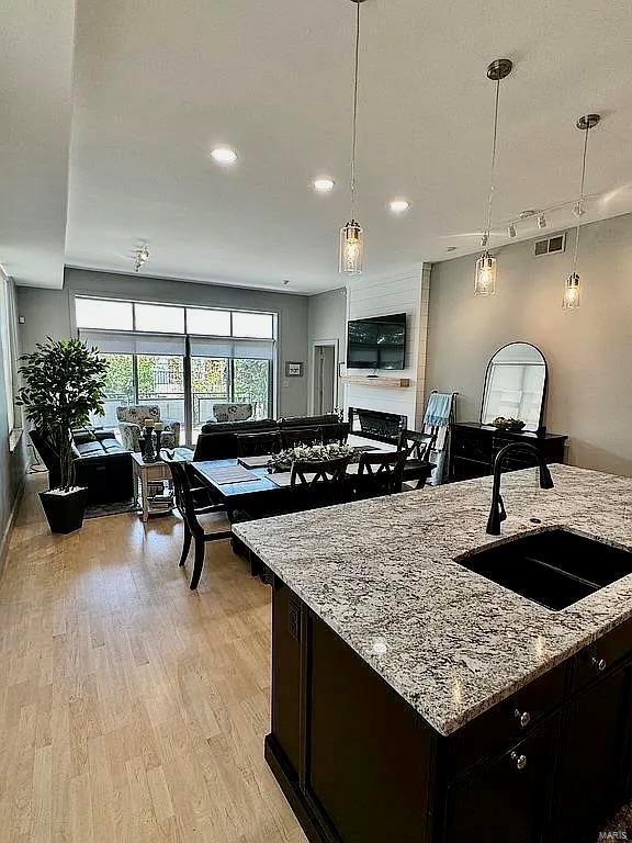 kitchen with hanging light fixtures, light stone countertops, light hardwood / wood-style floors, sink, and a kitchen island with sink