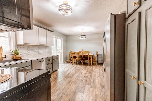 kitchen with appliances with stainless steel finishes, light hardwood / wood-style floors, white cabinets, backsplash, and pendant lighting