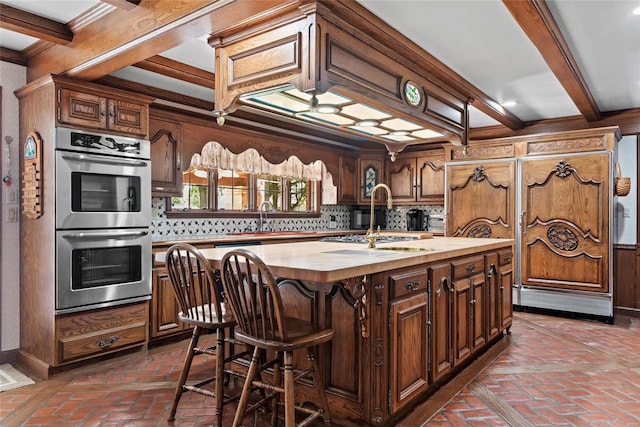 kitchen featuring appliances with stainless steel finishes, decorative backsplash, butcher block countertops, beamed ceiling, and a center island with sink