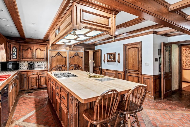 kitchen with beam ceiling, sink, butcher block countertops, a center island with sink, and black appliances