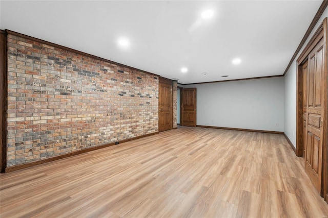 unfurnished room with brick wall, light wood-type flooring, a barn door, and ornamental molding