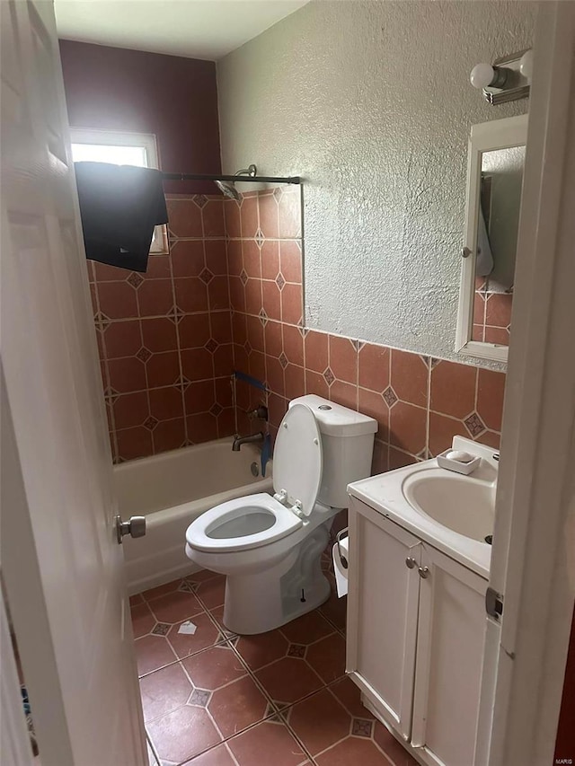 full bathroom with toilet, tile patterned flooring, vanity, tiled shower / bath combo, and tile walls