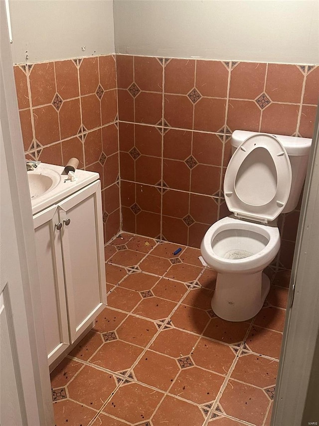 bathroom with vanity, toilet, and tile walls