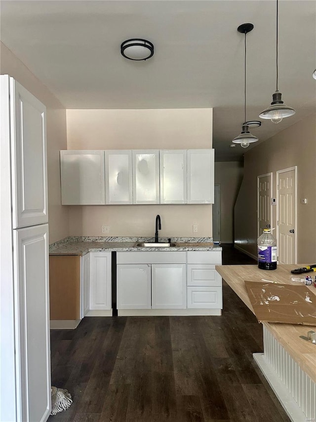 kitchen featuring white cabinets, light stone counters, sink, dark wood-type flooring, and pendant lighting