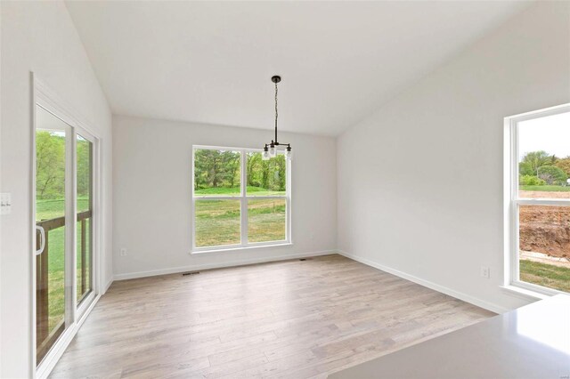 spare room with light wood-type flooring, a wealth of natural light, a chandelier, and vaulted ceiling