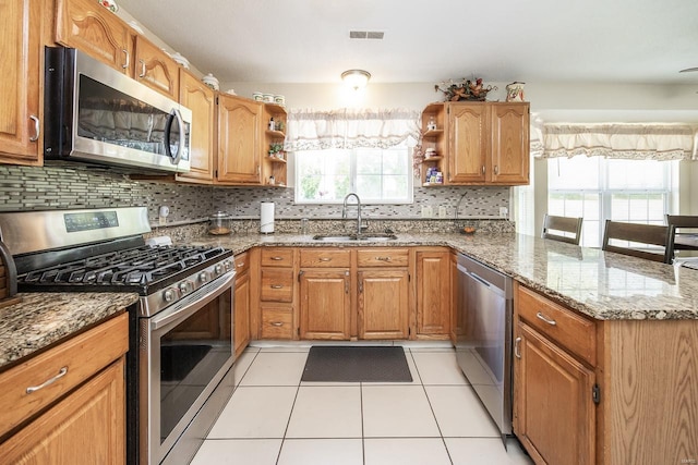 kitchen with dark stone countertops, stainless steel appliances, sink, and plenty of natural light