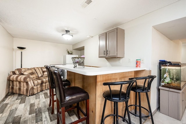 bar featuring gray cabinetry, light hardwood / wood-style floors, and white refrigerator