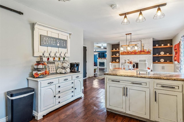 kitchen with built in shelves, dark hardwood / wood-style floors, light stone counters, and hanging light fixtures