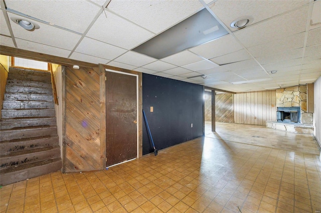 basement with wooden walls, a drop ceiling, and a fireplace