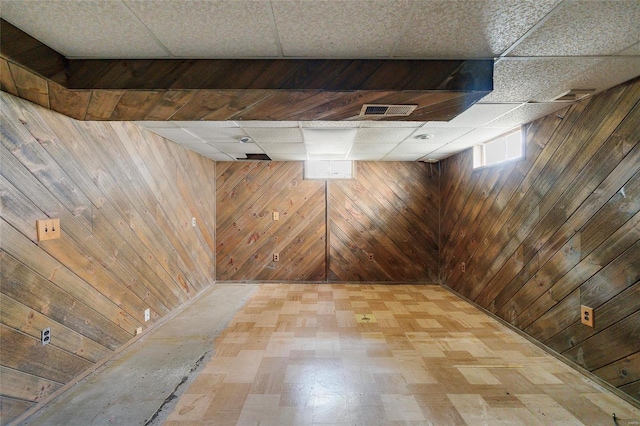 basement featuring wooden walls and a paneled ceiling